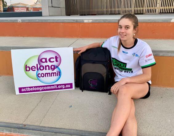 young female students sitting next to ACT BELONG COMMIT SIGN