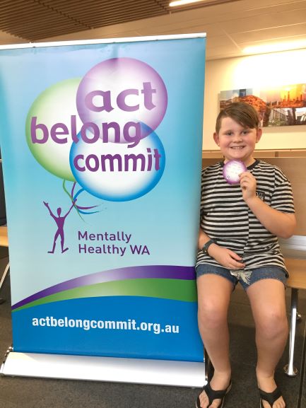 boy holding badge next to Act Belong Commit sign