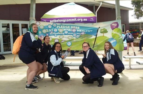 Students pointing to an Act Belong Commit banner