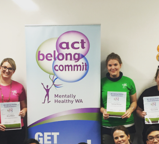 Participants of a course standing around an Act Belong Commit banner holding their certificates
