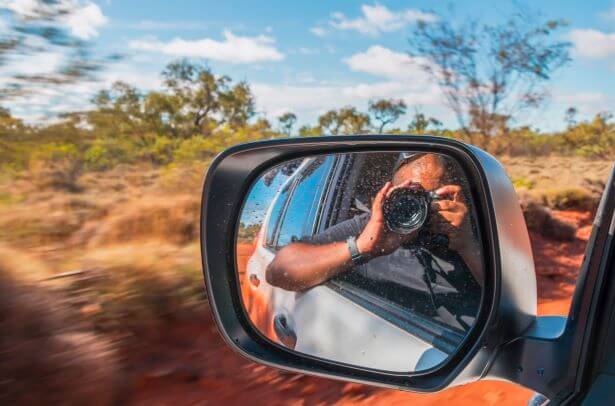 Man taking a photo out of a car window with his reflection in the wing mirror