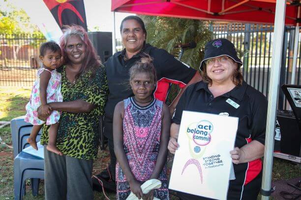 Aboriginal people outside with one lady holding an Act Belong Commit sign