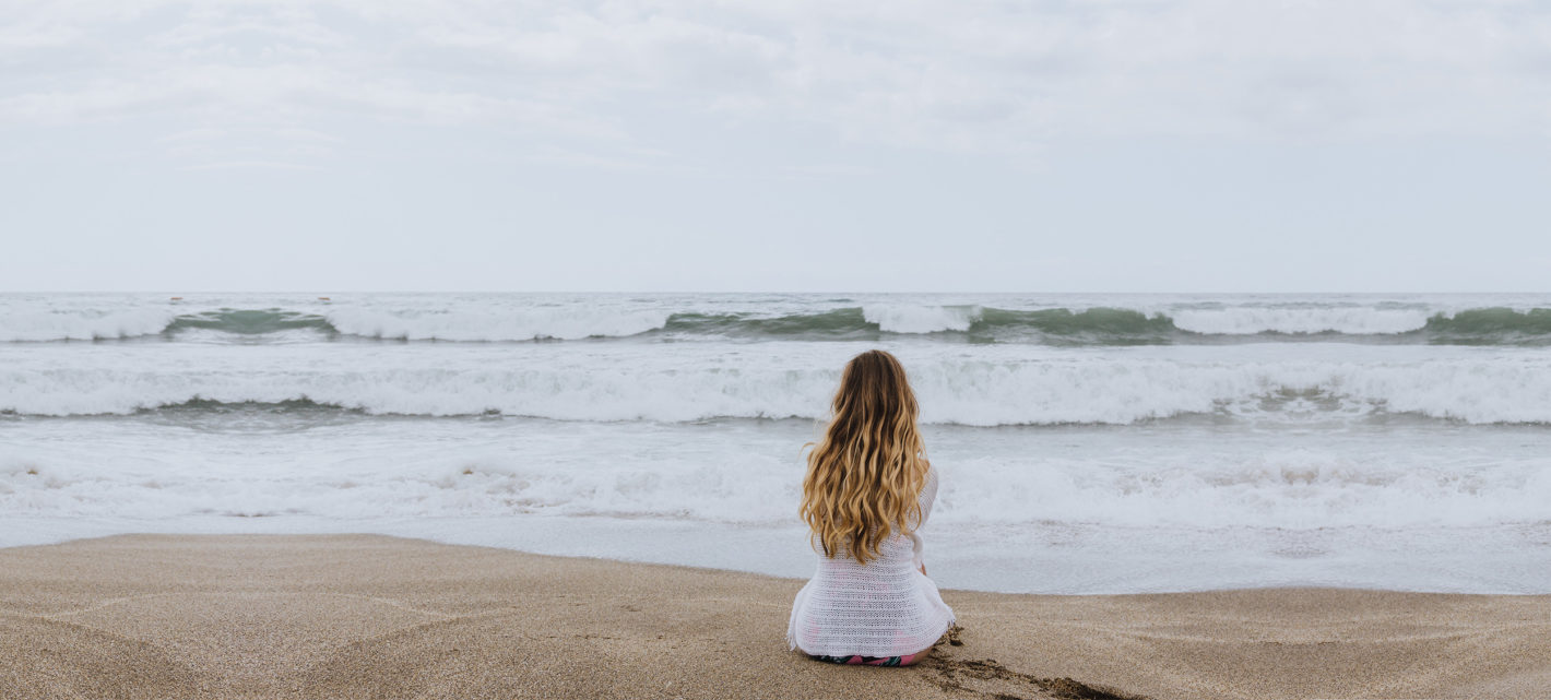 Young girl sitting on the beach looking at waves