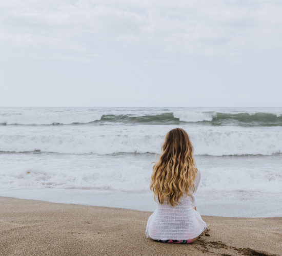 Young girl sitting on the beach looking at waves